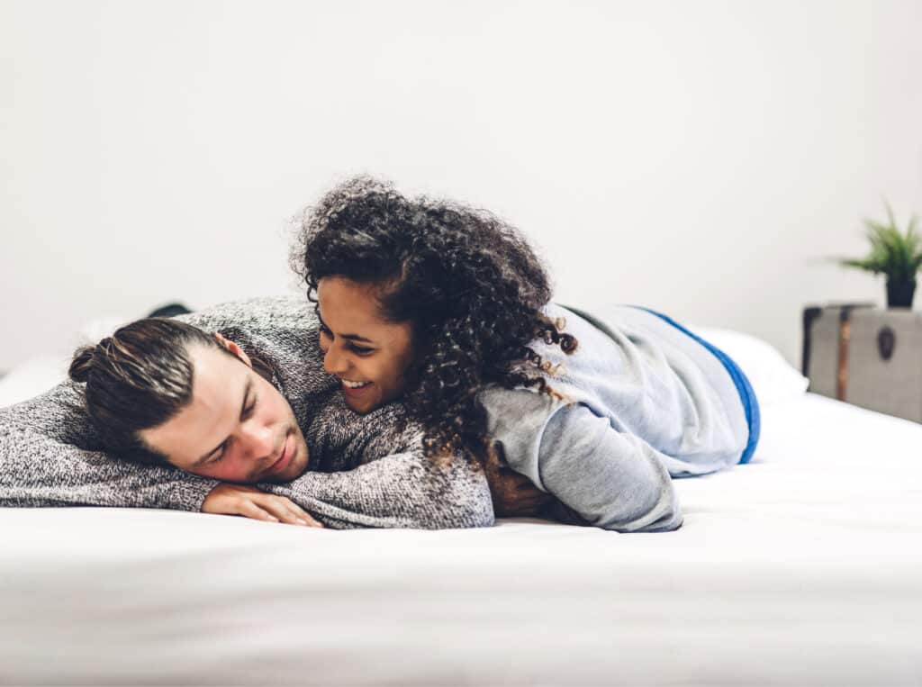Junges glückliches Paar liegt lachend gemeinsam im Bett, entspannt und kuschelt.