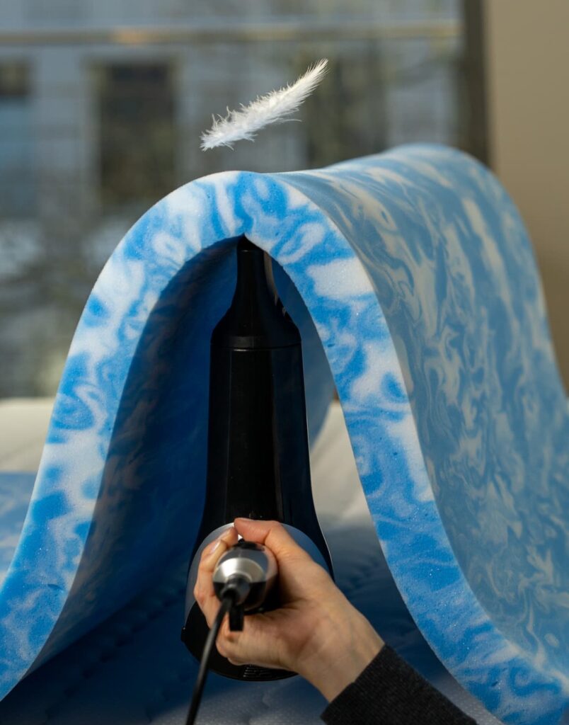 Hand hält Dampfreiniger vor atmungsaktives, blau-weiß gemustertes Textilmaterial