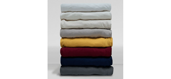 Stapelhaufen von Bettlaken in verschiedenen Farben: Hellblau, Grau, Gelb, Rot, Dunkelblau und Anthrazit.