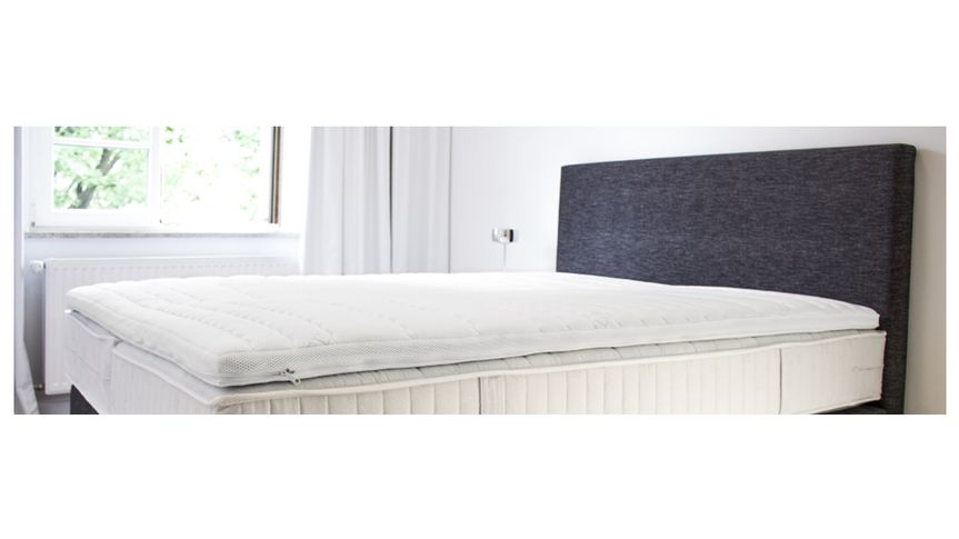 Eine weiße Topper-Auflage auf einer Matratze, mit gestepptem Bezug und leichtem, atmungsaktivem Material.