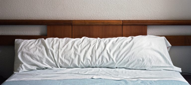 Ein Bett mit einem hölzernen Kopfteil und einem zerknitterten weißen Kissenbezug.