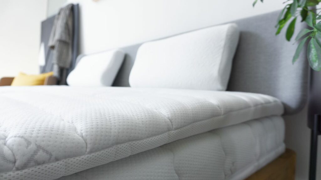 Detailaufnahme eines weißen Premium-Topper mit atmungsaktivem Bezug auf einem Bett, ergänzt durch zwei Kopfkissen.