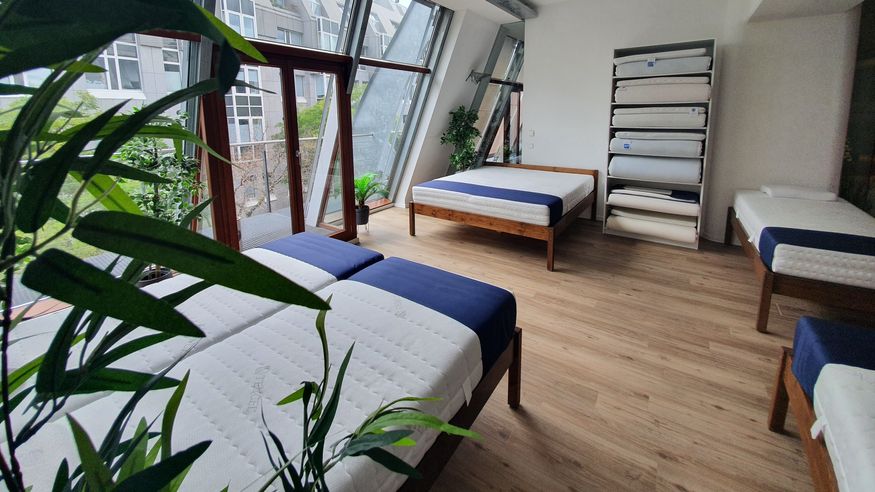 Schlafzimmer mit mehreren Betten und Matratzen in neutralen Farben, Holzrahmen und modernen Designs.