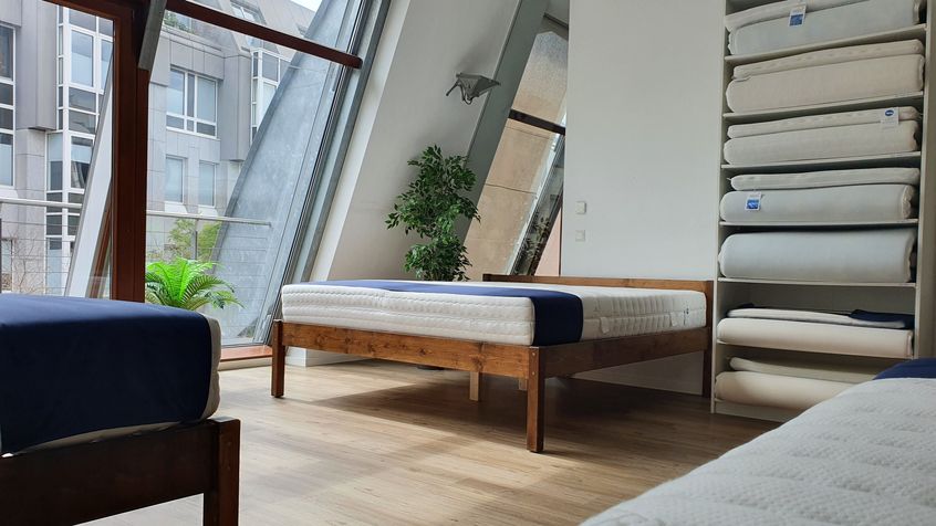Ein moderner Showroom mit Holzbetten und Matratzen in neutralen Farben, große Fenster sorgen für viel Licht.