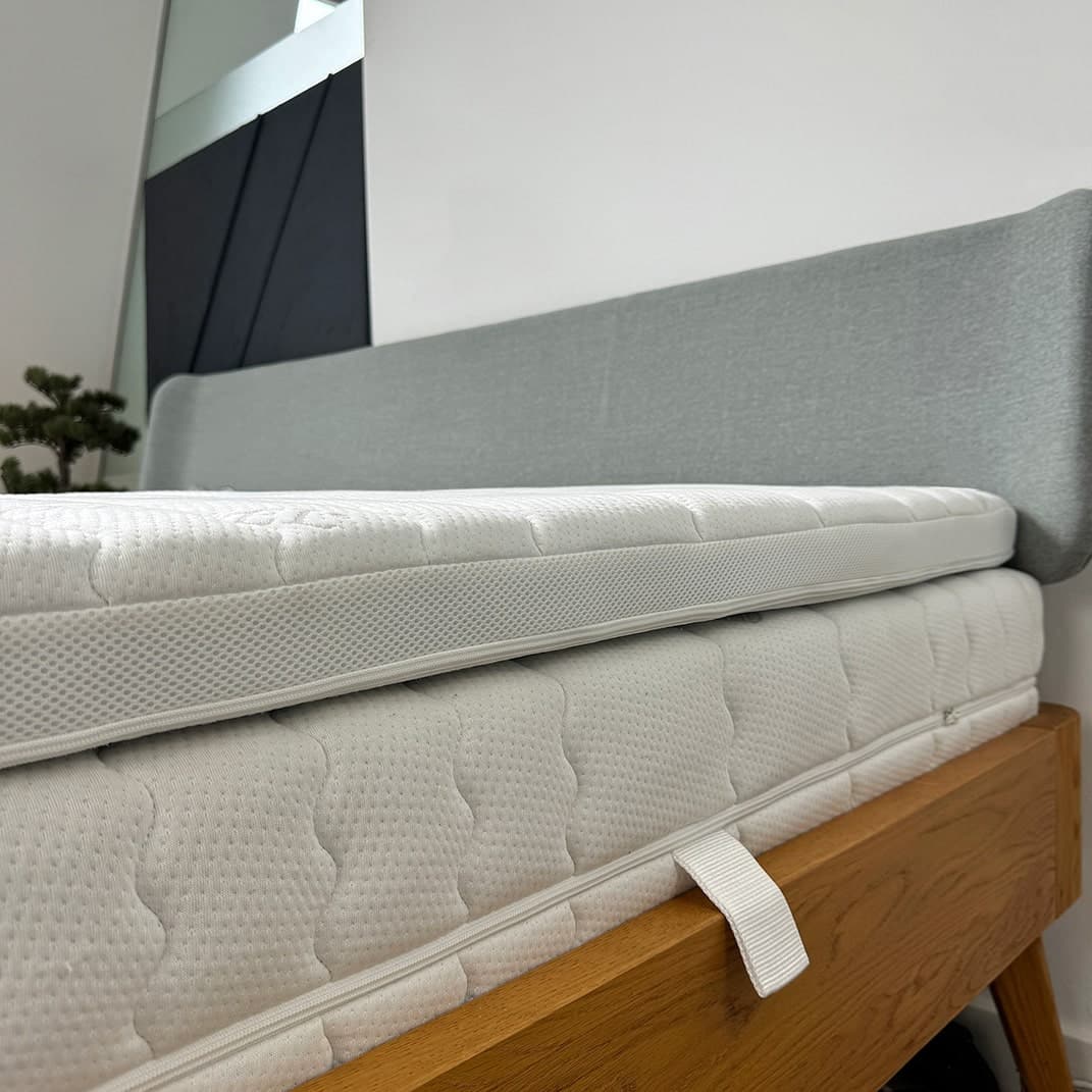 Doppelte Matratze in Weiß mit atmungsaktivem Bezug auf einem Holzrahmen, Kopfteil in grauem Stoff.