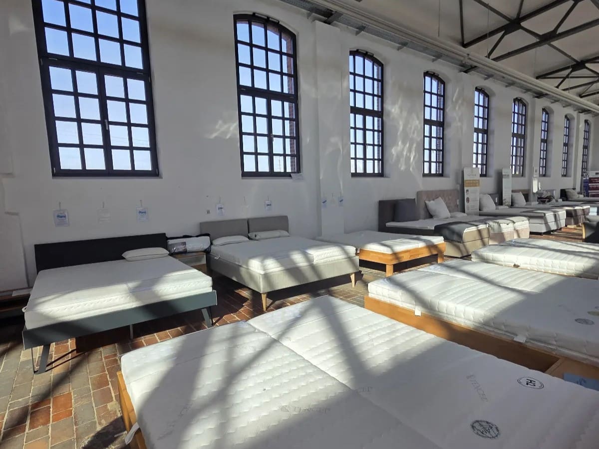 AM Qualitätsmatratzen Showroom mit verschiedenen Matratzen und Betten in neutralen Farben, ausgestattet mit Kopf- und Fußteilen.
