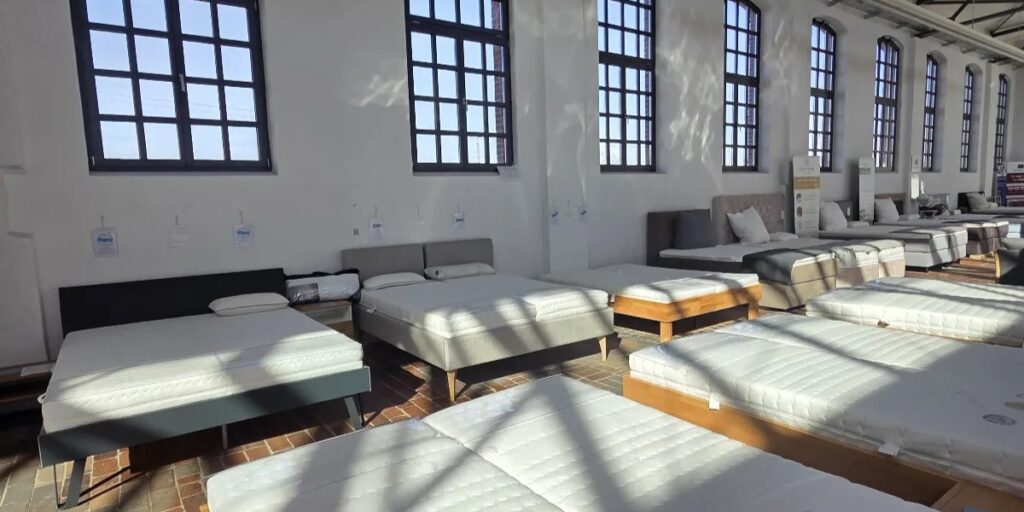Verschiedene Matratzen und Betten in einem modernen Showroom in Berlin von AM QUalitätsmatratzen, hell erleuchtet mit großen Fenstern.