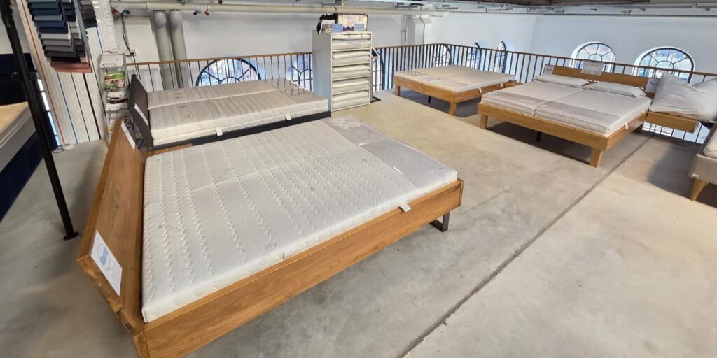 Mehrere Betten mit Holzrahmen und Matratzen in einem Showroom von AM Qualitätsmatratzen in München, helles Design und klare Linien.